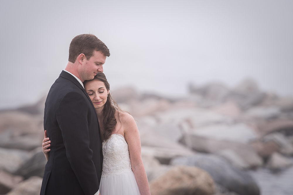 Bride and Groom hugging on rocks on beach in the fog
